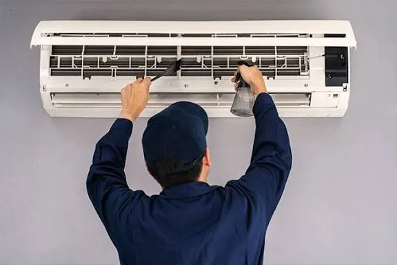 Technician cleaning and maintaining an indoor air conditioning unit